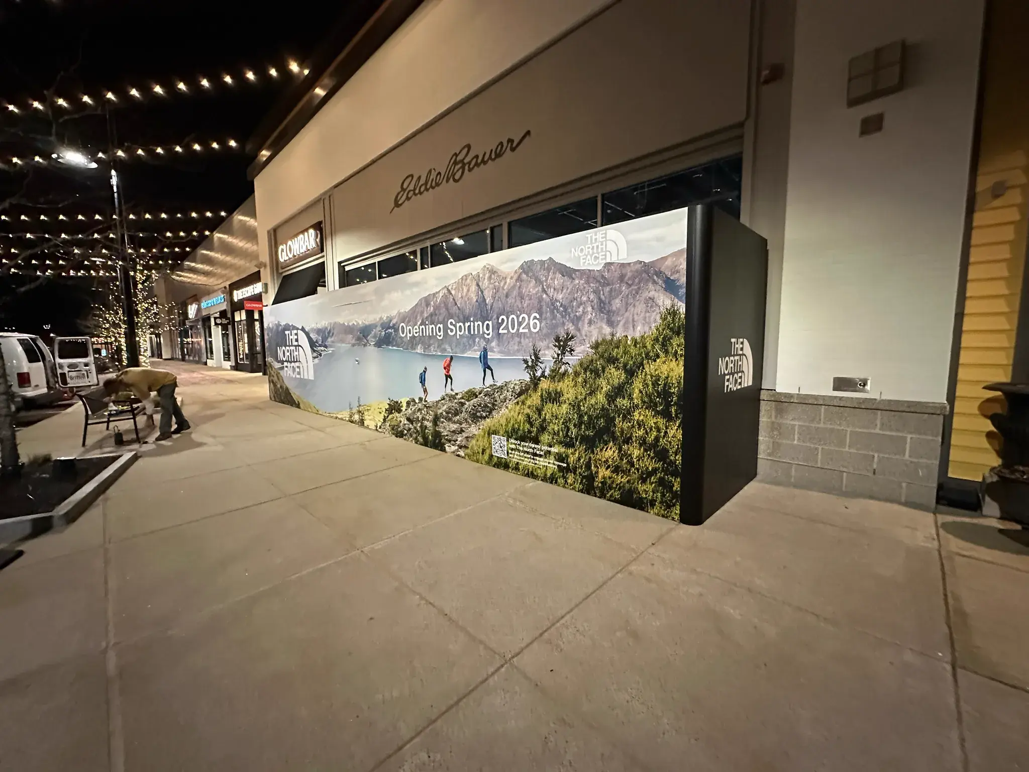 The North Face hoarding at night with a worker at a bench alongside