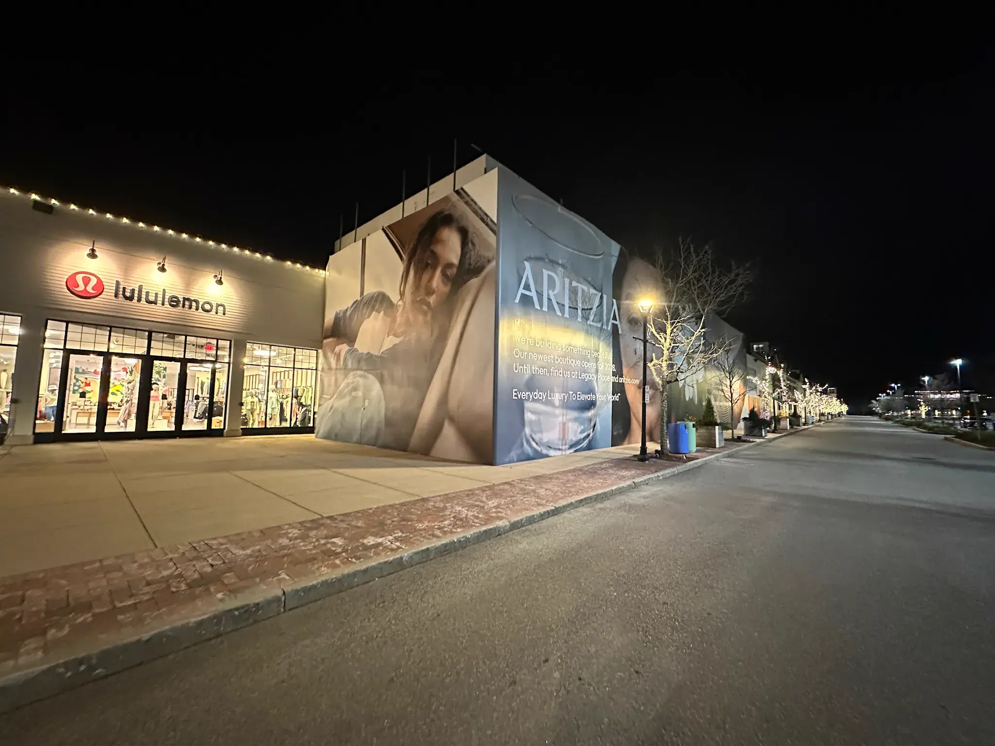 Aritzia hoarding graphic wrapping a building corner beside a lululemon storefront
