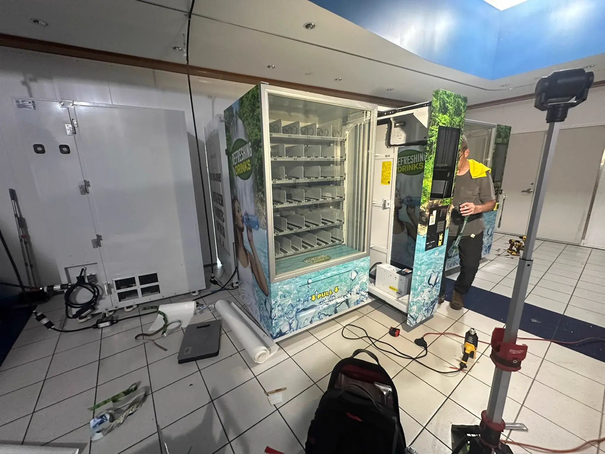 Installer beside two wrapped vending machines with drills and media on the floor