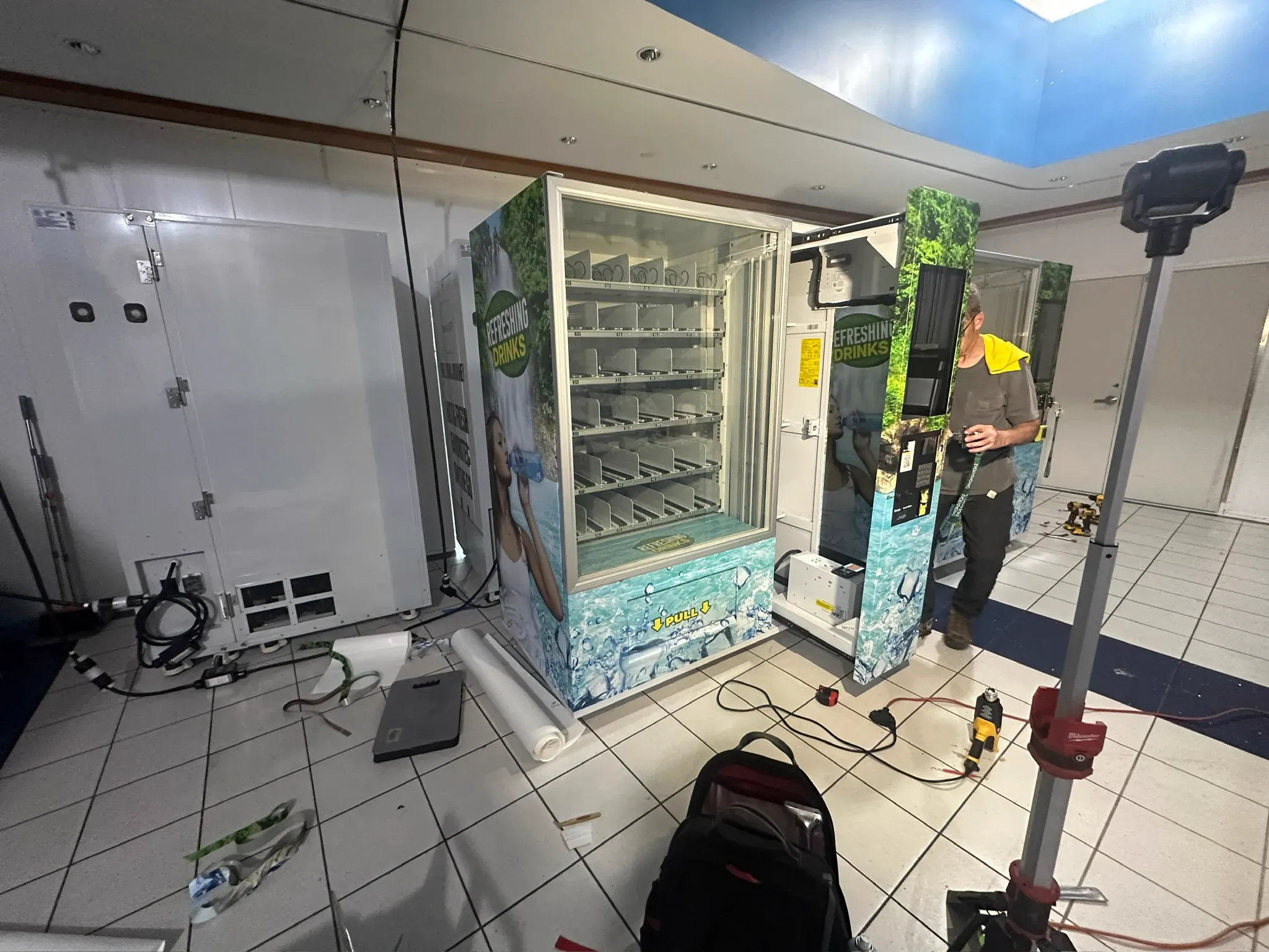 Installer beside two wrapped vending machines with tools on the floor