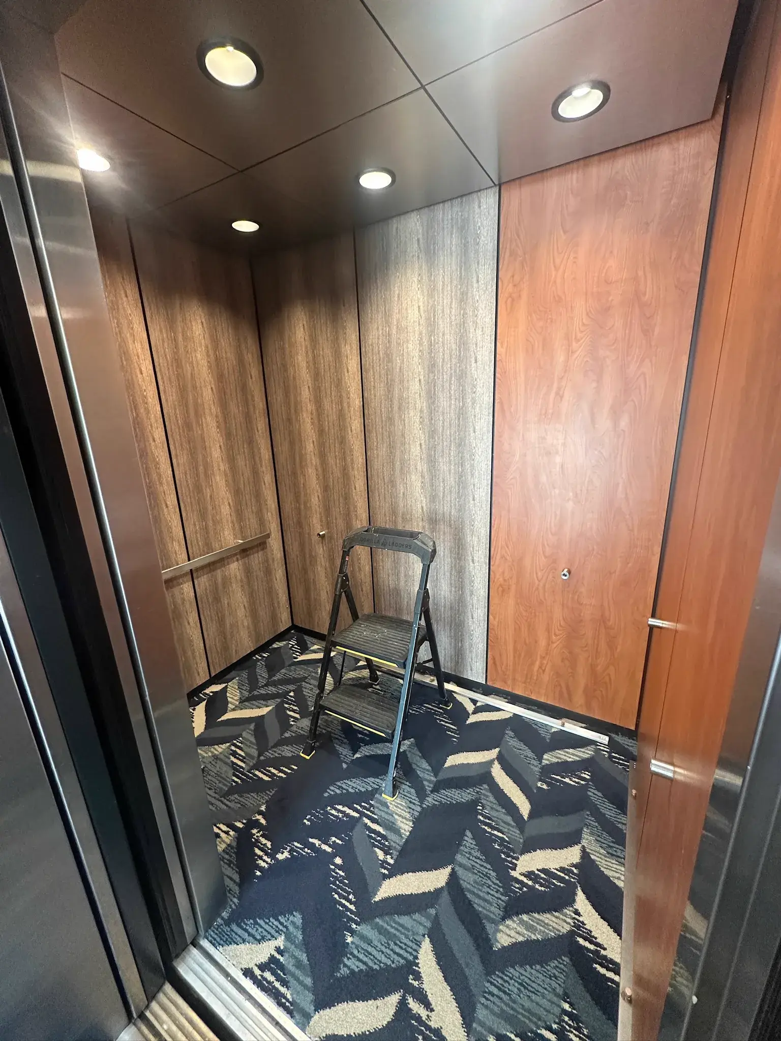 Elevator cab interior with wood grain wrapped panels and a step ladder inside